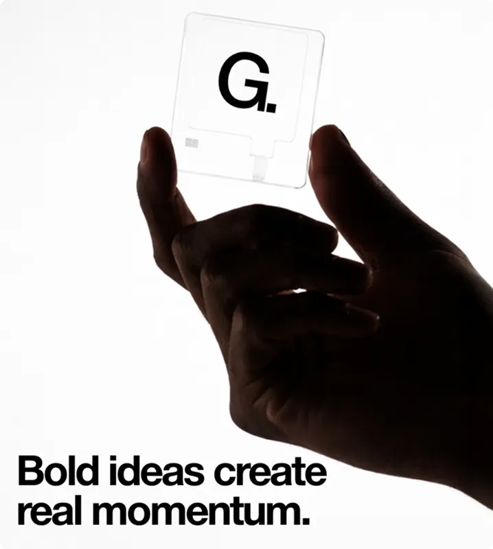 Eine Hand hält eine transparente Karte mit einem schwarzen Großbuchstaben G und Punkt, darunter der Text ‚Bold ideas create real momentum.‘