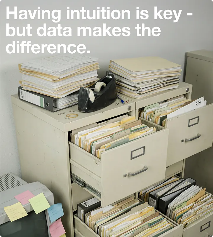 Beige Aktenschrank mit geöffneten Schubladen, voll mit Ordnern und Akten, darauf liegen Stapel von Dokumenten und ein Klebebandabroller; Text: Intuition ist wichtig, aber Daten machen den Unterschied.