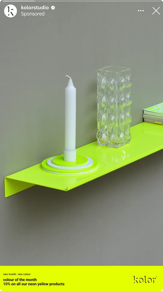 Neongelbes Wandregal mit weißer Kerze auf rundem Halter, klarem Glasbehälter und Büchern an einer grauen Wand.