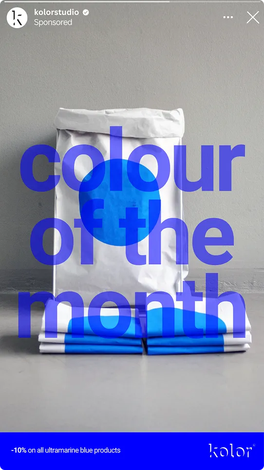 Weiße Papiertüte mit blauem Kreis steht hinter vier gestapelten Schokoladentafeln in Ultramarinblau, Text darüber 'colour of the month'.