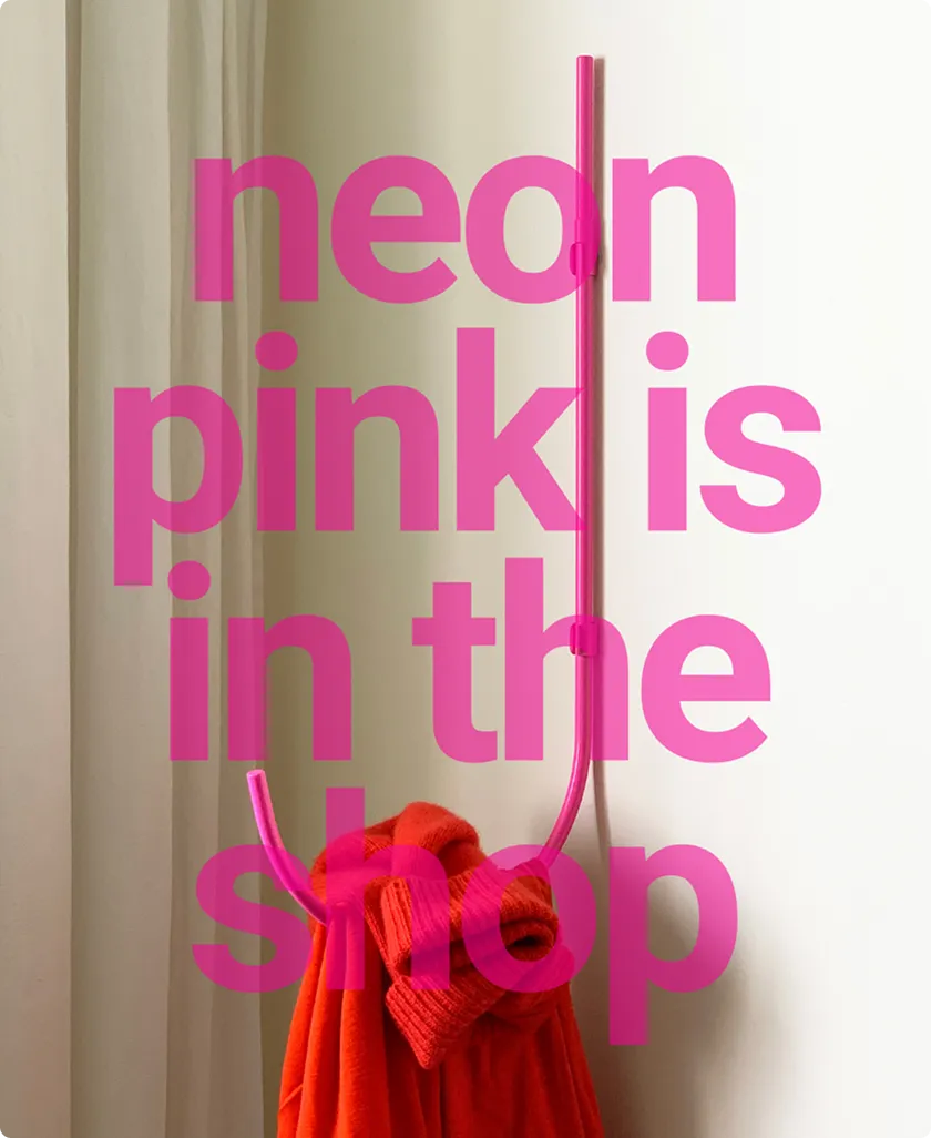 Neonpinkfarbener Wandhaken mit rotem Pullover und Vorhängen im Hintergrund.