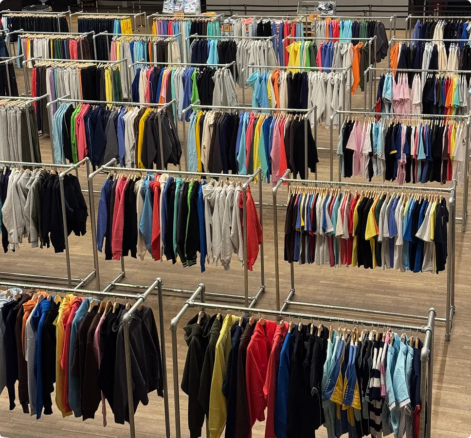 Viele bunte Sweatshirts und T-Shirts hängen auf Metallkleiderständern in einem großen, offenen Raum mit Holzfußboden.