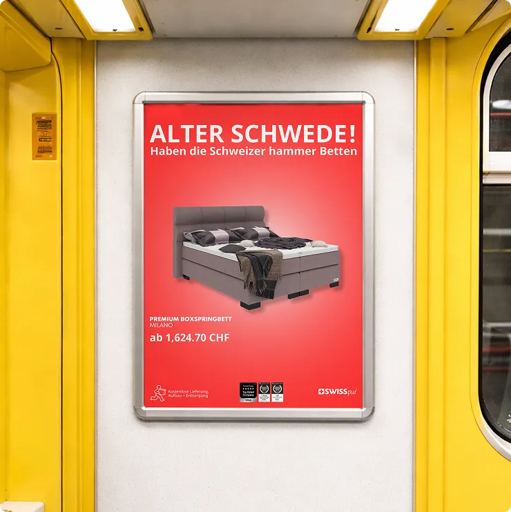 Werbeplakat in einer gelben U-Bahn mit einem grauen Boxspringbett vor rotem Hintergrund und dem Text "Alter Schwede! Haben die Schweizer hammer Betten".