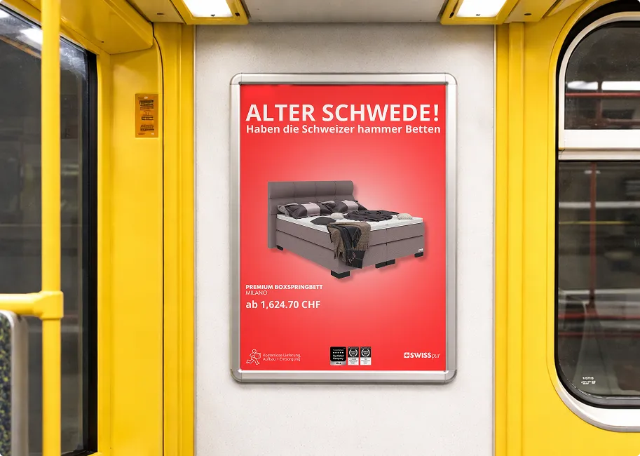 Anzeige in einem gelben Zug zeigt ein graues Premium-Boxspringbett Milano mit Kissen und Decke, Preis ab 1.624,70 CHF, mit dem Slogan 'Alter Schwede! Haben die Schweizer hammer Betten'.
