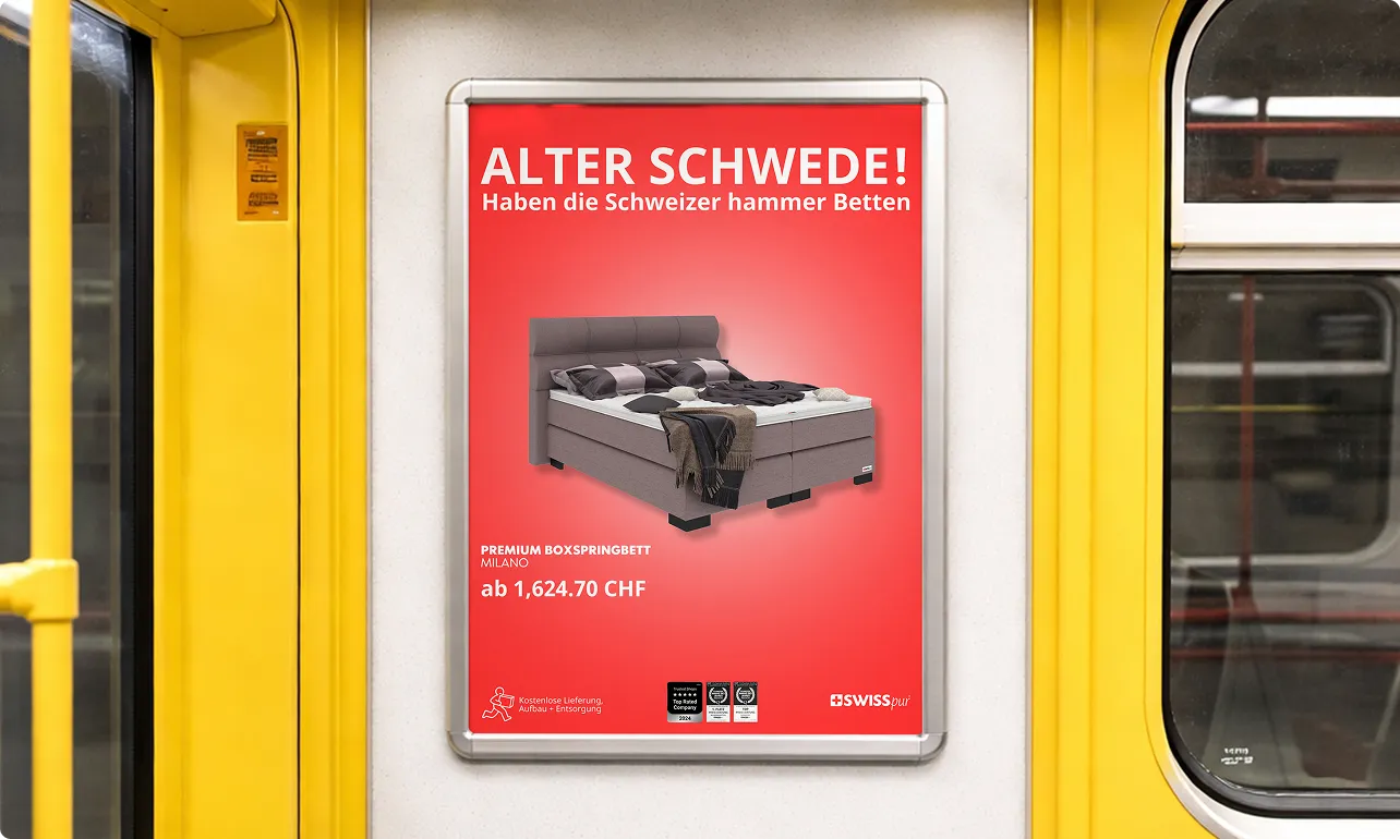 Werbeplakat in einer U-Bahn mit einem grauen Boxspringbett-Modell Milano und dem Text ‚Alter Schwede! Haben die Schweizer hammer Betten‘ in Weiß auf rotem Hintergrund.