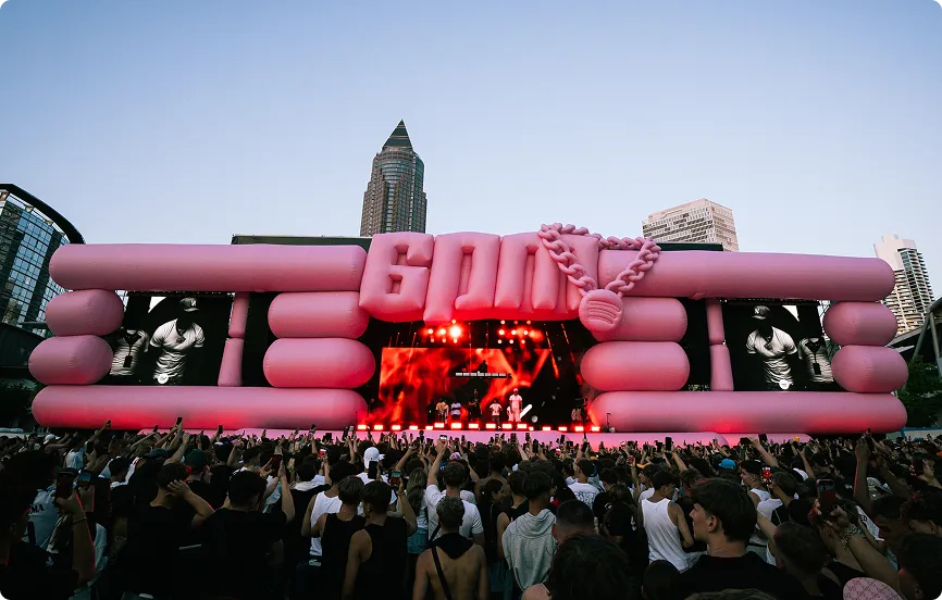 Große Menschenmenge bei einem Open-Air-Konzert vor einer Bühne mit großer aufblasbarer rosa Dekoration und der Aufschrift ‚6000‘.