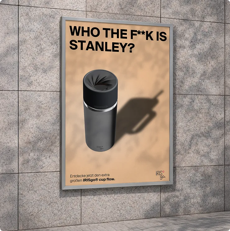 Wer zum Teufel ist Stanley? Werbung für den IRISgo Becher mit großem Cup-Flow, dargestellt auf einer Wand aus grauen Steinfliesen.