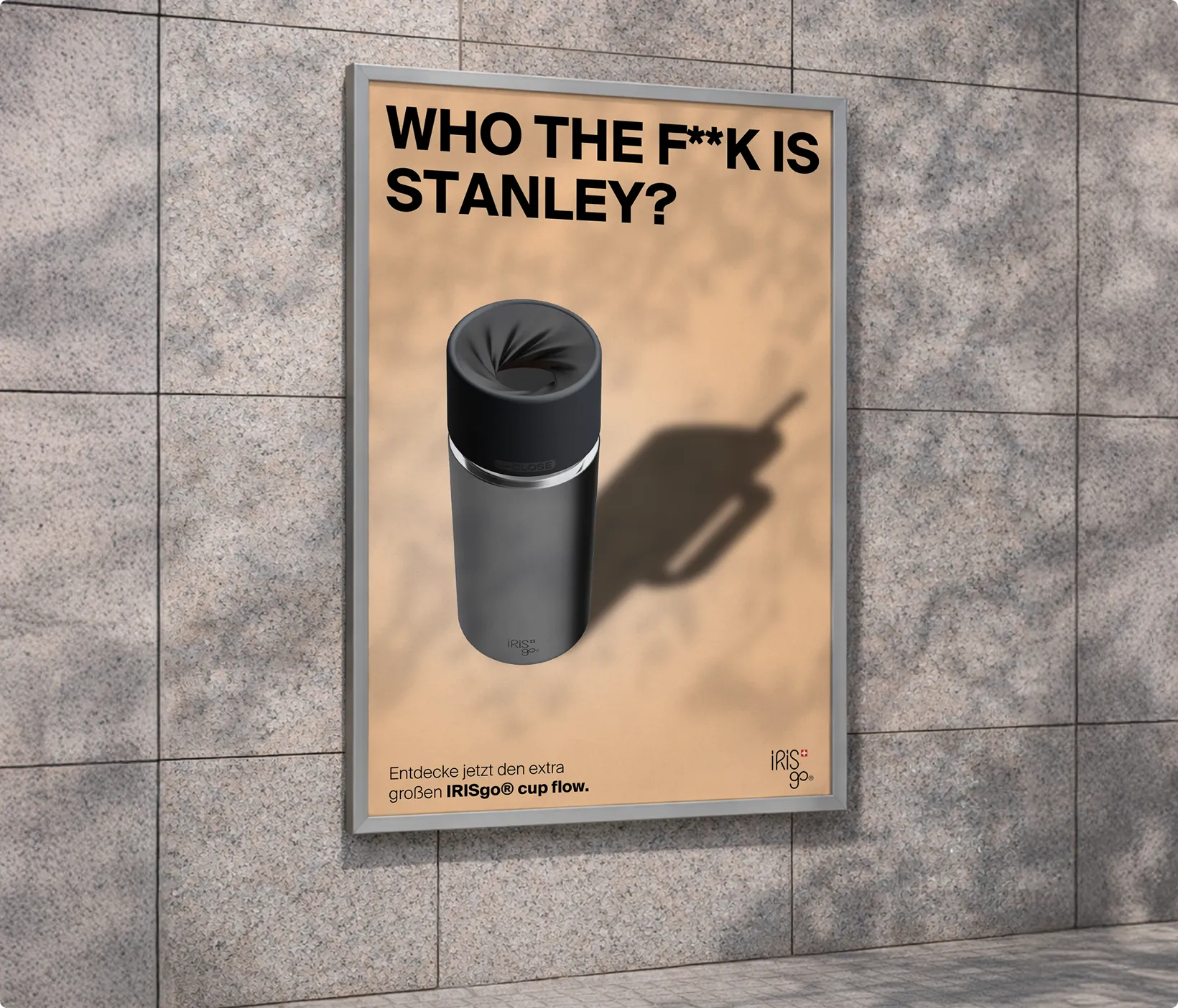 Wer zum Teufel ist Stanley? Anzeige mit schwarzem IRISgo® cup flow Becher vor beigem Hintergrund an Wand.