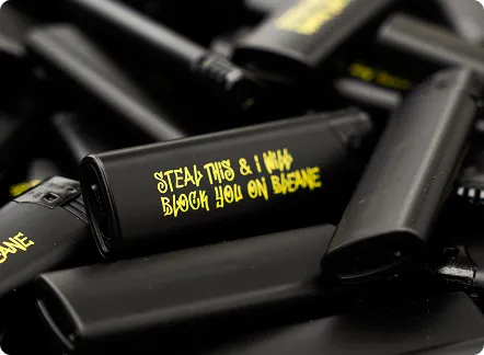 Mehrere schwarze Pfefferspray-Dosen, eine mit der gelben Aufschrift ‚STEAL THIS & I WILL BLOCK YOU ON BUSSANE‘.