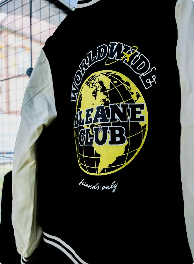 Rückseite einer schwarzen und weißen Jacke mit dem gelben Globus-Logo und dem Text ‚WORLDWIDE BLEANE CLUB friends only‘.