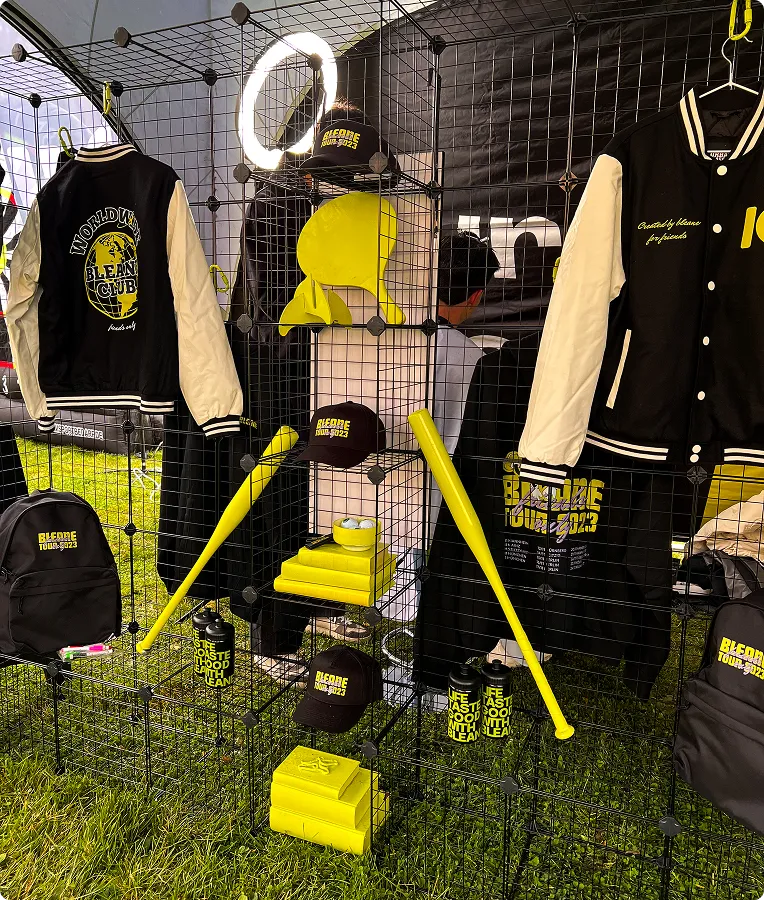 Schwarze und gelbe Baseball-Accessoires und Kleidung, darunter Jacken, Kappen, Schläger und Trinkflaschen, auf einem schwarzen Gitterständer im Freien ausgestellt.