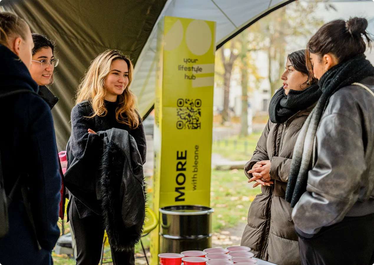 Fünf Frauen stehen in einer halb offenen Zelthalle und unterhalten sich, vor ihnen steht ein Tisch mit mehreren roten Bechern.
