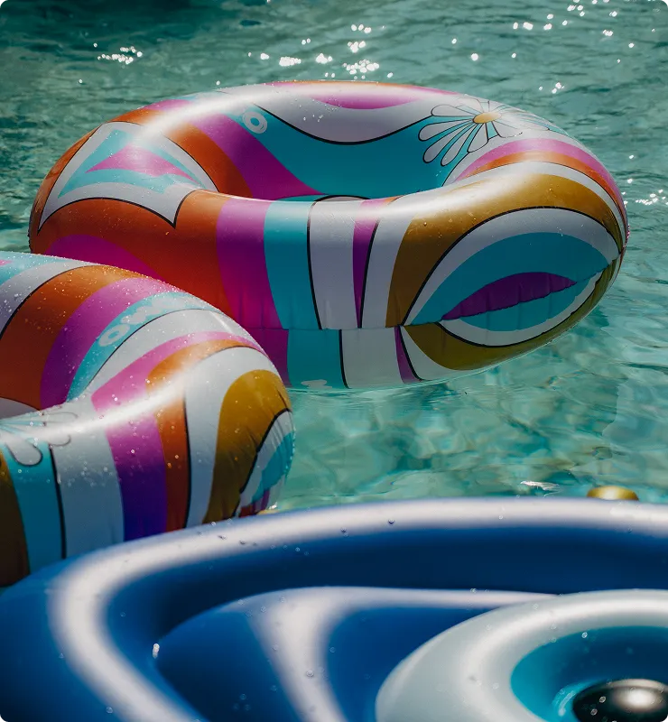 Bunte Schwimmreifen mit Streifen und Blumenmuster schwimmen auf klarem Wasser.