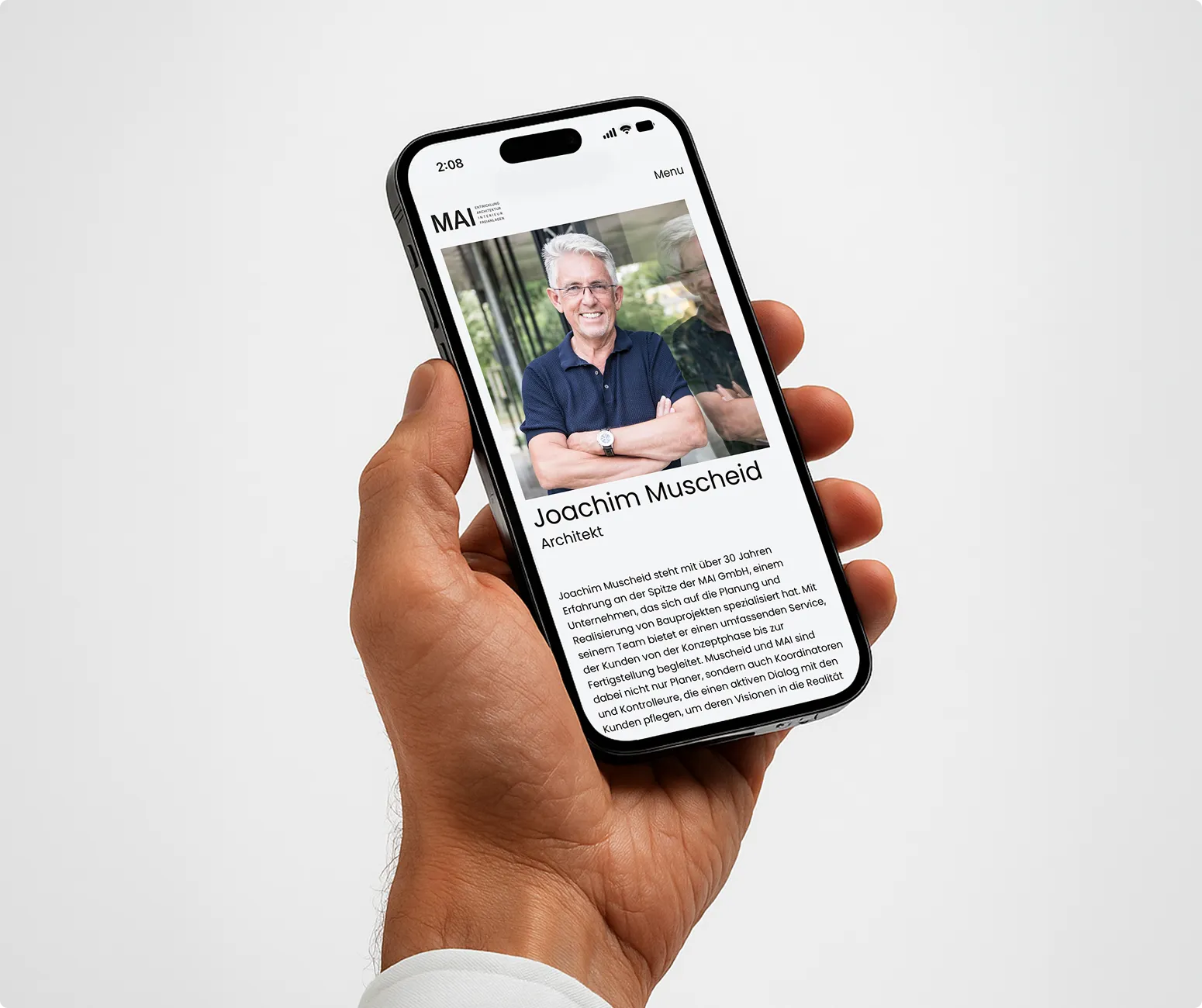 Hand hält ein Smartphone mit der Profilseite von Joachim Muscheid, einem älteren Mann mit grauen Haaren und Brille, auf dem Bildschirm.