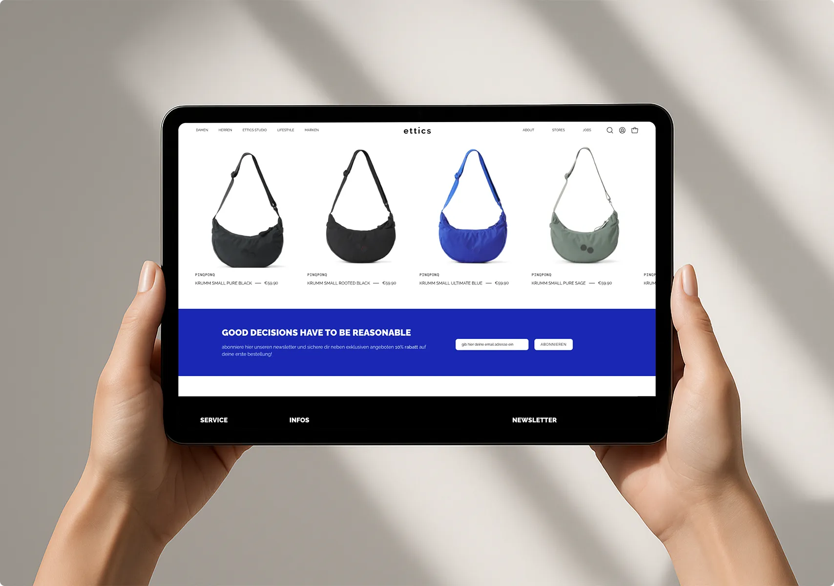 Tablet in Händen zeigt eine Website mit vier Umhängetaschen in Schwarz, Blau und Grau, darunter Newsletter-Anmeldung mit blauem Hintergrund.