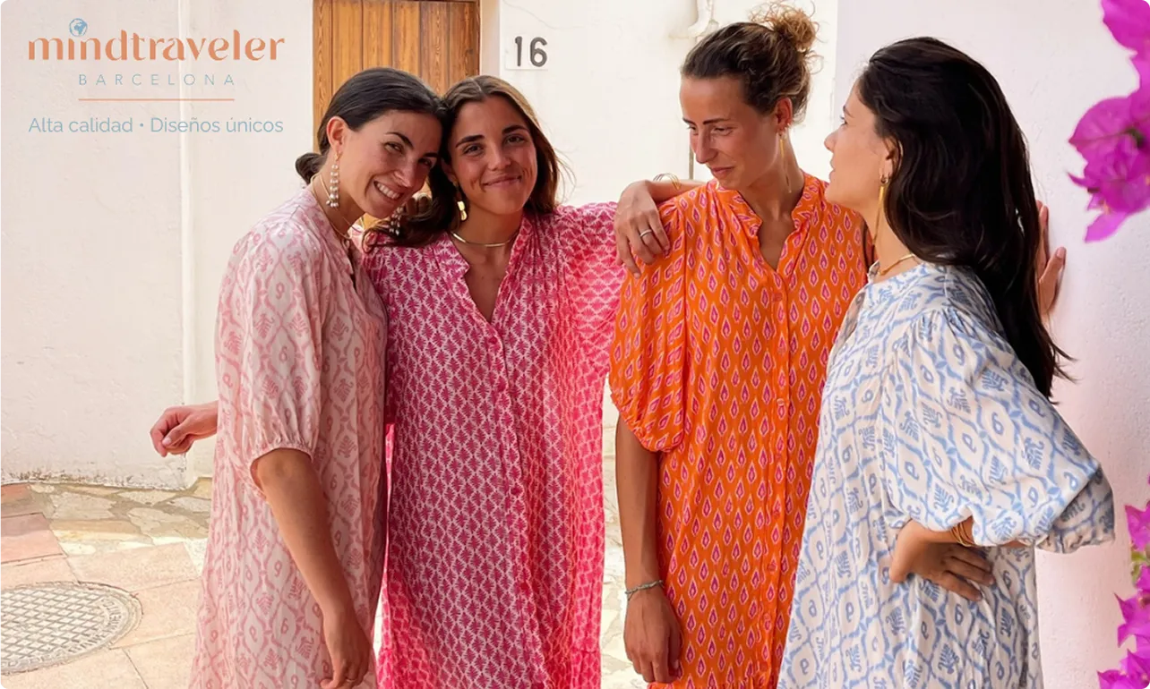 Vier Frauen in bunten, gemusterten Kleidern lehnen entspannt an einer weißen Wand mit der Hausnummer 16.