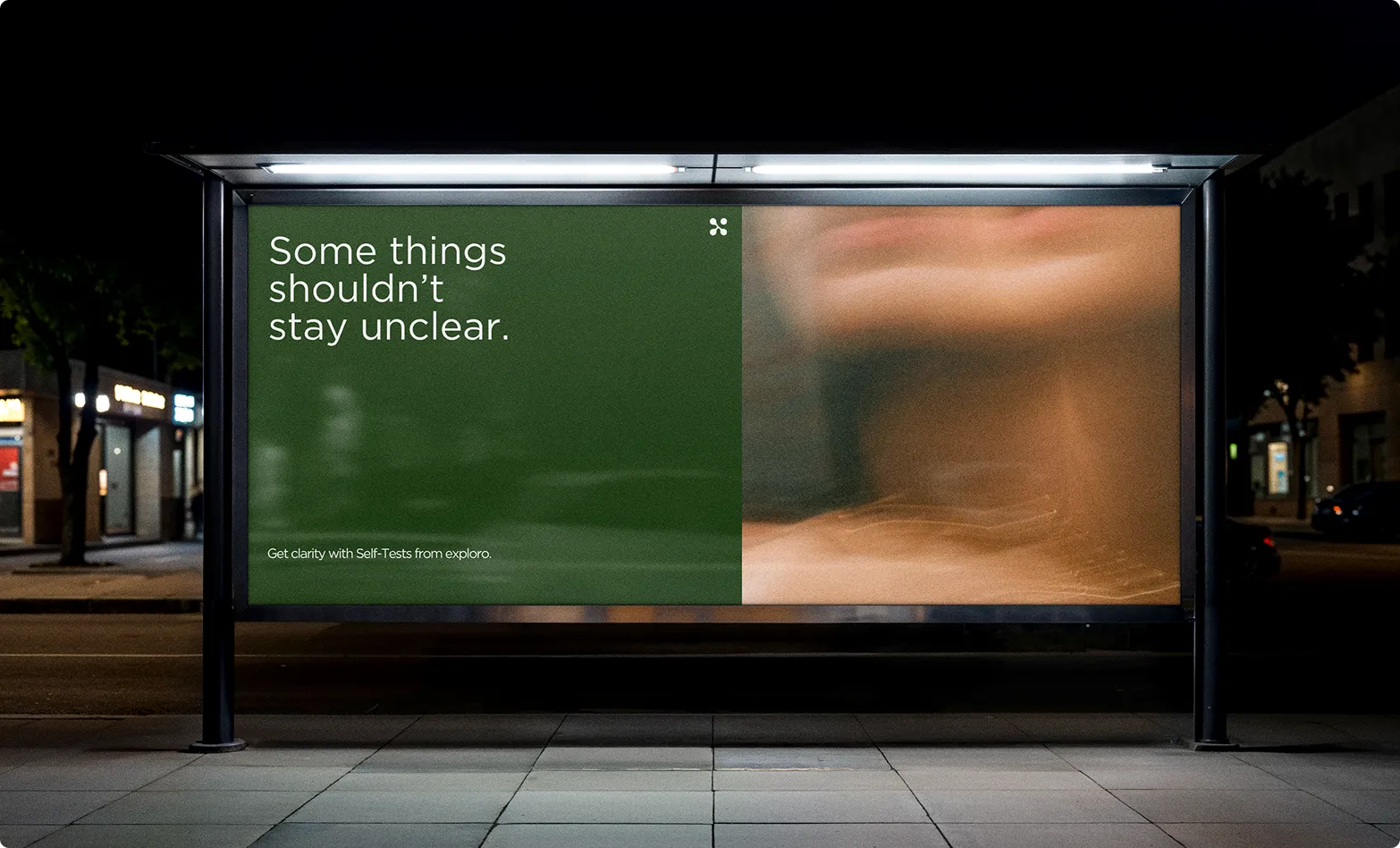 Werbetafel an einer Bushaltestelle bei Nacht mit Text 'Some things shouldn't stay unclear' auf grünem Hintergrund und verschwommenem Bild daneben.