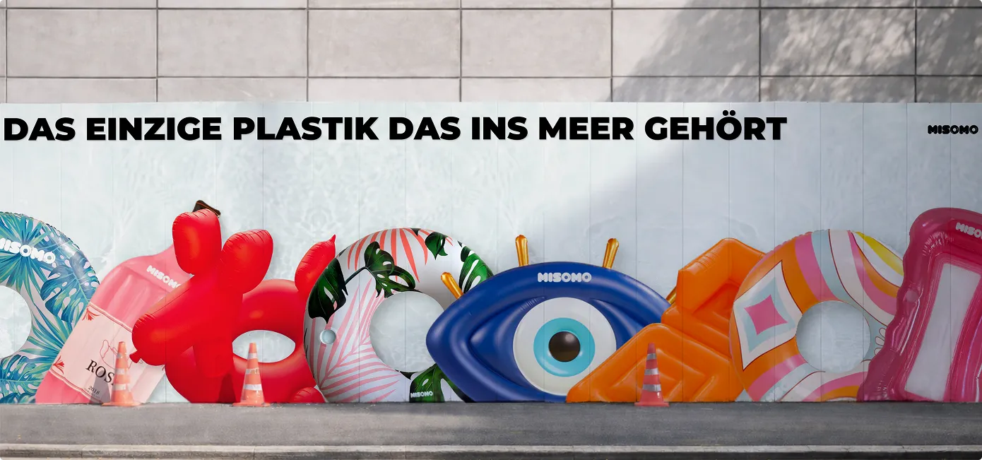 Wand mit aufgereihten bunten aufblasbaren Schwimmringen und Schwimmmatten neben der Aufschrift: Das einzige Plastik das ins Meer gehört.