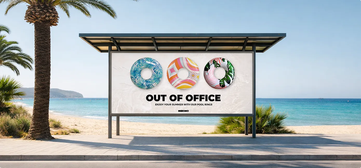 Werbetafel am Strand mit drei bunten Schwimmreifen und dem Text 'Out of Office – Genieße deinen Sommer mit unseren Schwimmringen'.