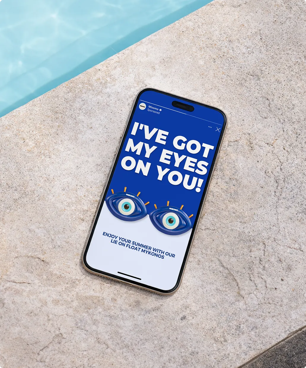 Smartphone auf Steinboden neben Pool zeigt Werbung mit Text 'I'VE GOT MY EYES ON YOU!' und zwei blauen Schwimmringen in Augenform.