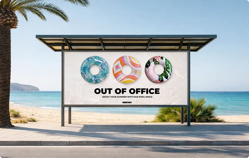 Werbetafel am Strand mit drei bunten Schwimmreifen und dem Text ‚Out of Office – Genießen Sie Ihren Sommer mit unseren Schwimmringen‘.