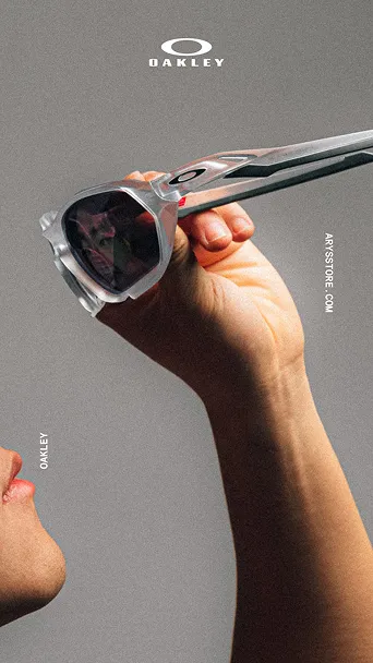 Hand hält eine silberne Oakley-Sonnenbrille vor das Gesicht vor grauem Hintergrund.