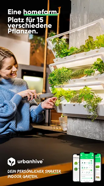 Frau in blauem Pullover pflegt Kräuter und Pflanzen in einem vertikalen Indoor-Garten mit mehreren Fächerfächern an einer Wand.