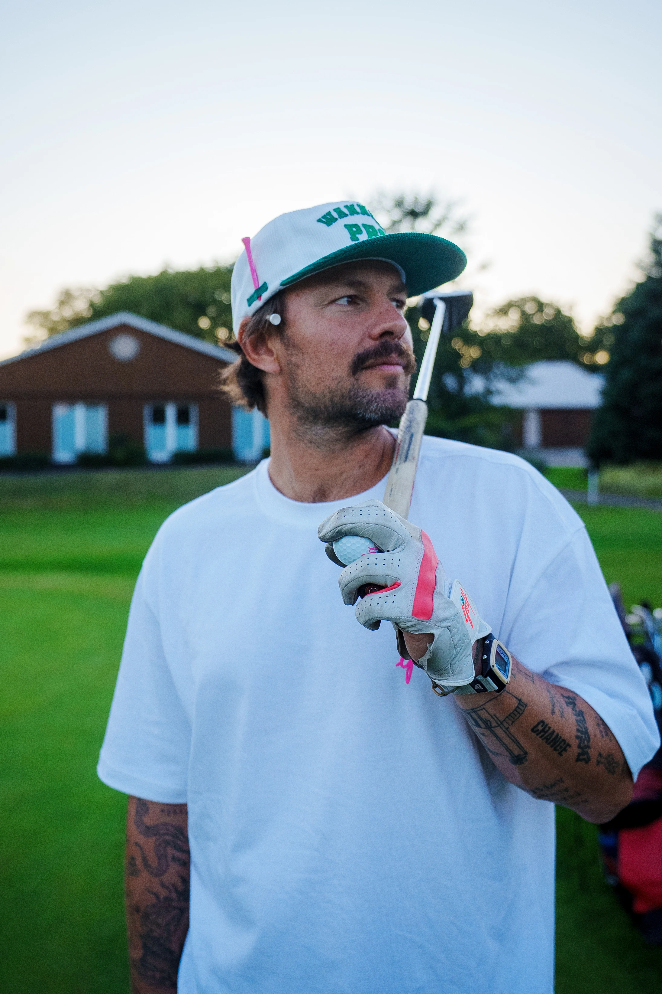 Mann mit Baseballkappe und Handschuh hält Golfschläger und Golfball auf einer Golfwiese.