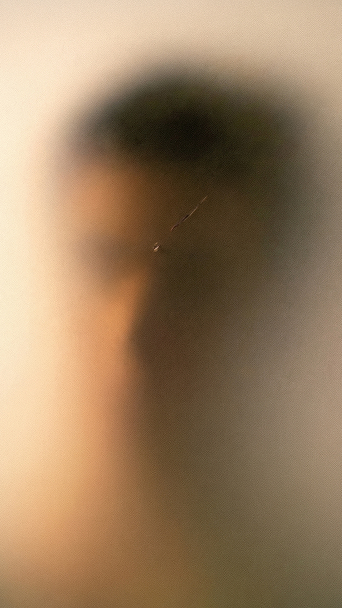 Unscharfes, verschwommenes Porträt eines nach links blickenden Menschen hinter mattiertem Glas.