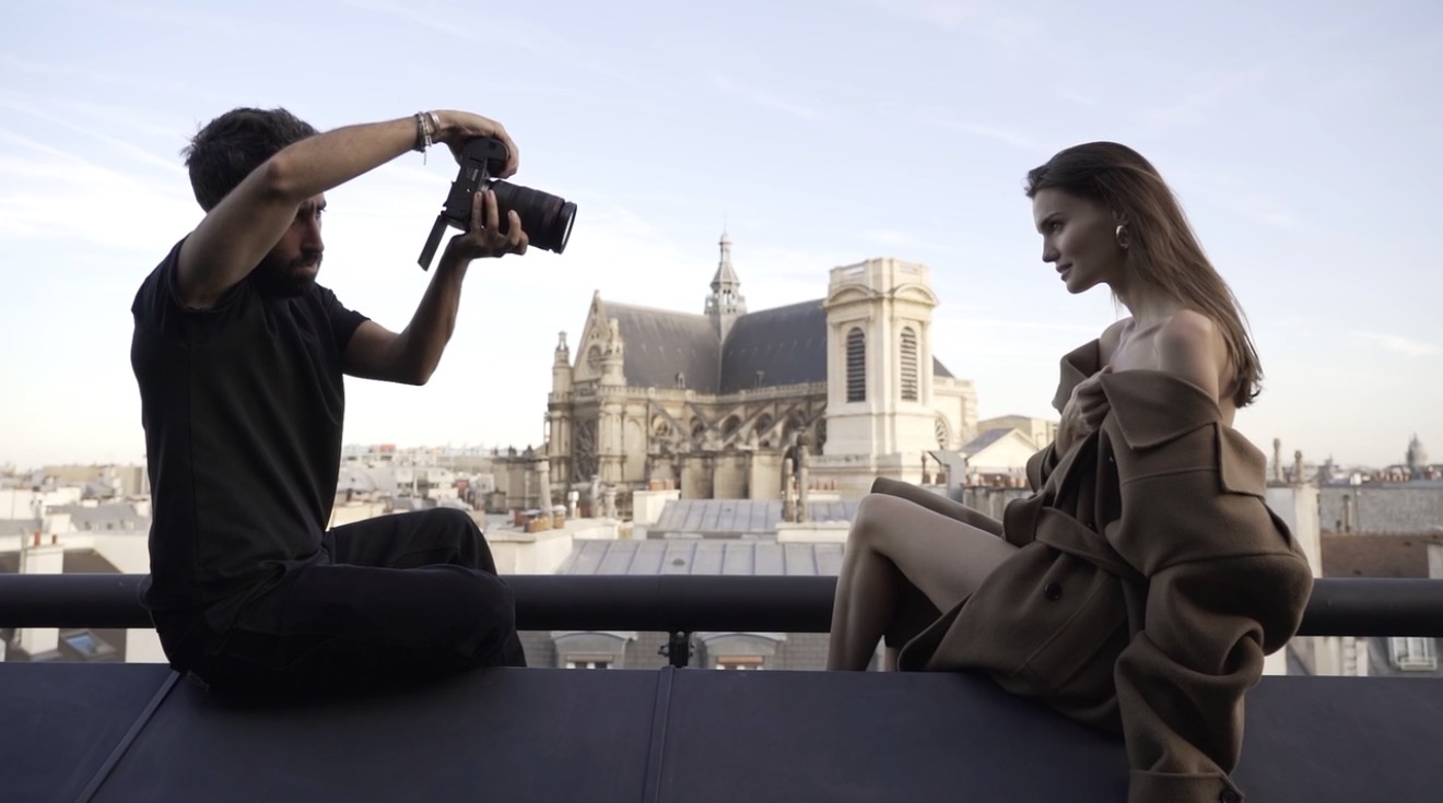 Mann fotografiert Frau, die auf Dach mit historischem Gebäude im Hintergrund posiert.