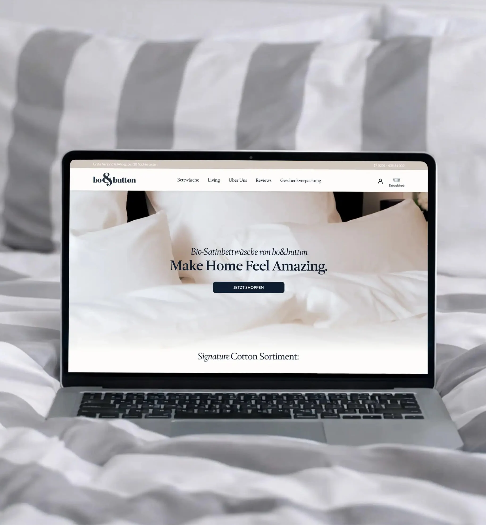 Laptop auf einem Bett mit weißer Bettwäsche zeigt Webseite von bo&button mit Bio-Satinbettwäsche und Slogan Make Home Feel Amazing.