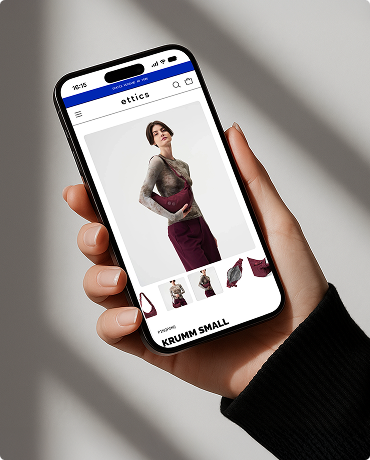 Hand hält Smartphone mit geöffneter Website, die eine Frau zeigt, die eine kleine dunkelrote Tasche trägt, Modellname KRUMM SMALL.
