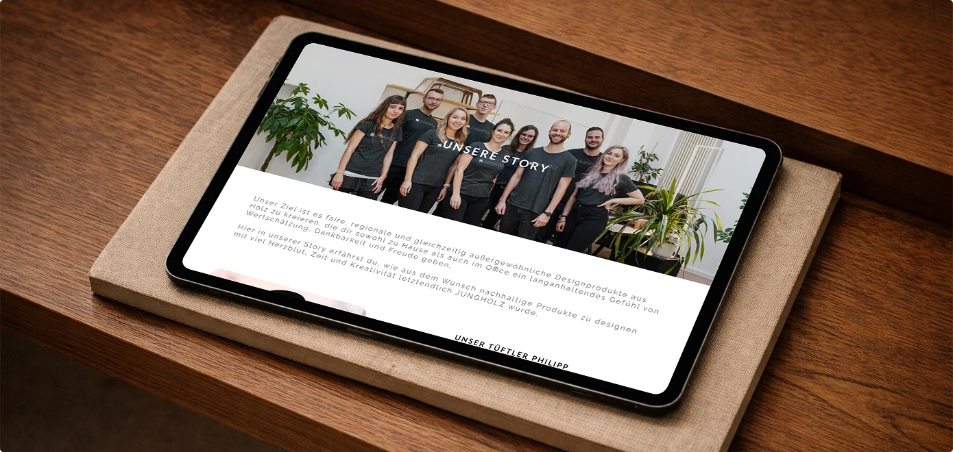 Tablet zeigt eine Webseite mit Bild eines Teams von neun Personen vor weißen Wänden und Pflanzen mit der Überschrift 'Unsere Story' und Text über nachhaltige Designprodukte aus Holz.