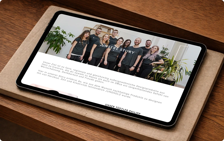 Tablet zeigt ein Teamfoto von neun Personen in schwarzen T-Shirts mit dem Text 'UNSERE STORY' und einem deutschen Absatz über nachhaltige, regionale Holzdesignprodukte.