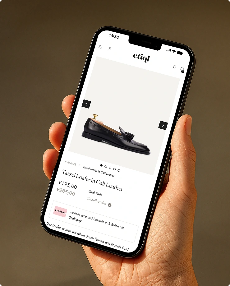 Hand hält ein Smartphone mit einer Produktseite für einen schwarzen Tassel Loafer aus Kalbsleder und einem Preis von 195 Euro.