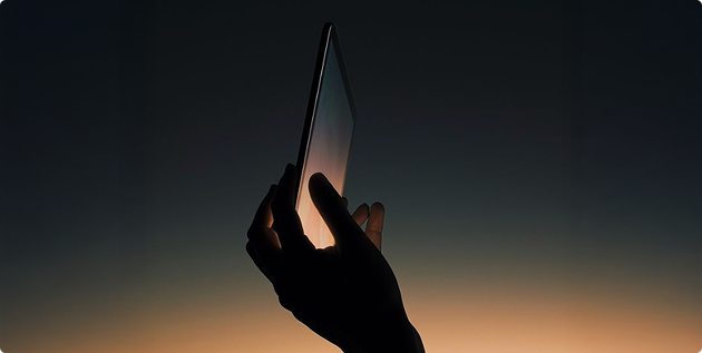 Hand hält ein Smartphone gegen einen dunklen Himmel mit orangefarbenem Sonnenuntergang.