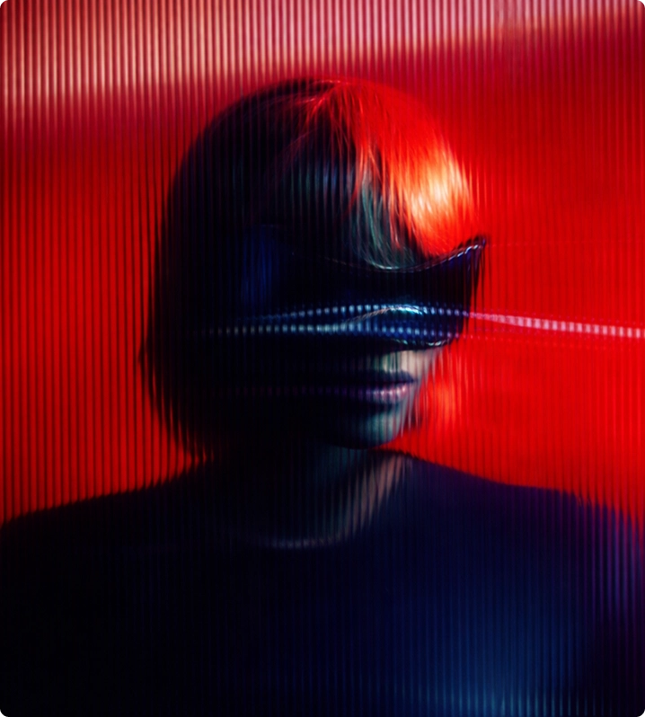 Person mit kurzem Haar trägt eine futuristische, reflektierende Brille vor rotem Hintergrund.