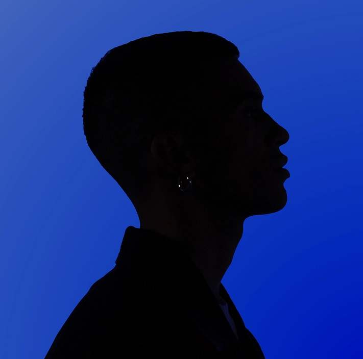 Silhouette eines jungen Mannes mit kurzem Haar und Ohrring vor blauem Hintergrund.