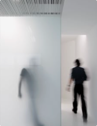 Zwei unscharfe Personen gehen in einem modernen, minimalistischen Innenraum mit weißen Wänden und Deckenpaneelen.