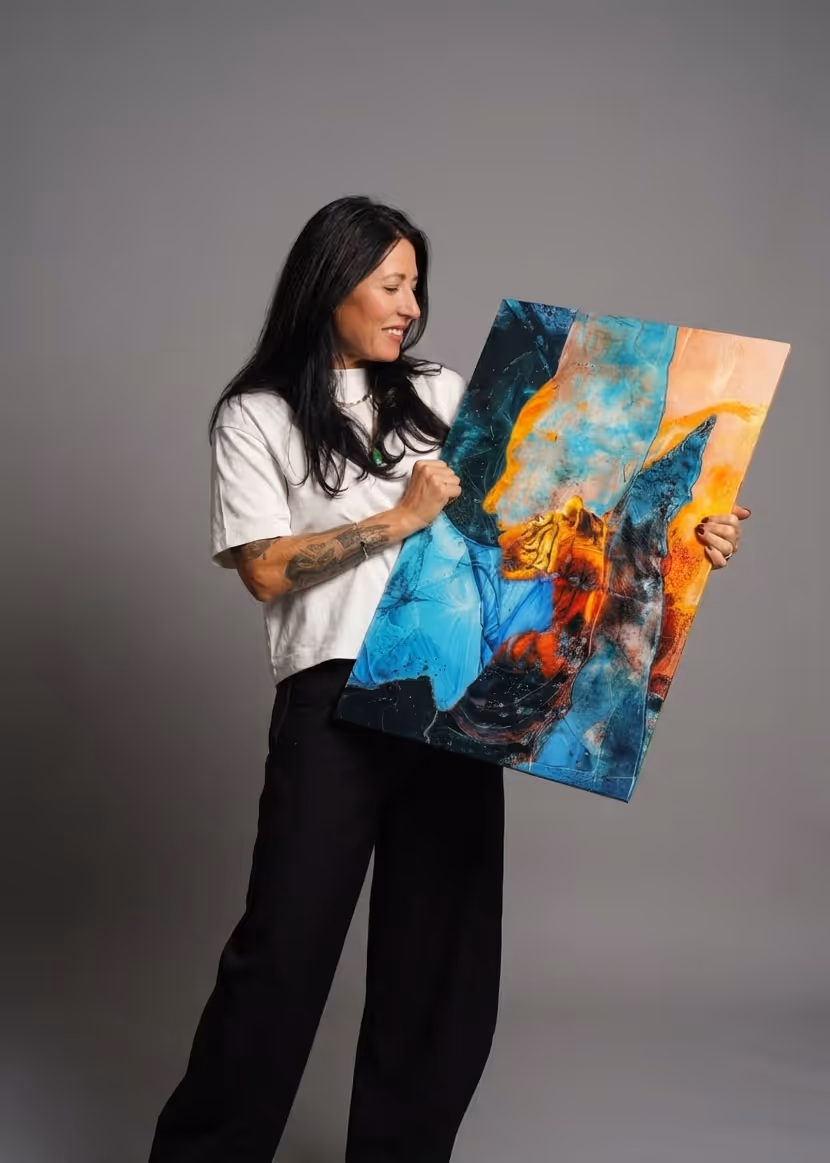 Frau mit langen dunklen Haaren, die ein farbenfrohes, abstraktes Gemälde mit Blau-, Gelb- und Orangetönen hält.