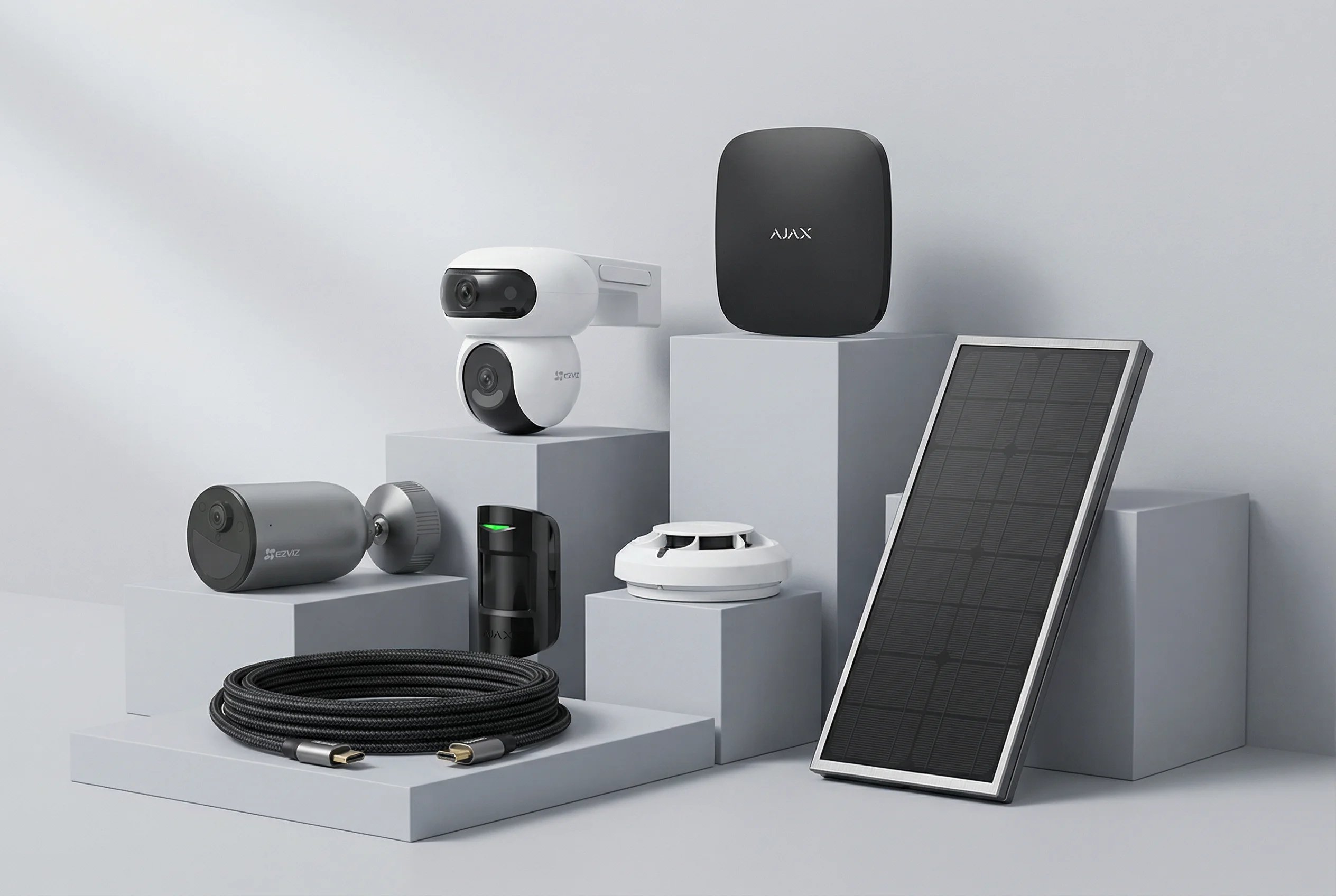Collection of security devices including surveillance cameras, a motion sensor, a smoke detector, a solar panel, and a braided cable displayed on gray blocks.