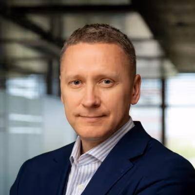 Portrait of a man in a blue suit jacket and striped shirt in a modern office setting.