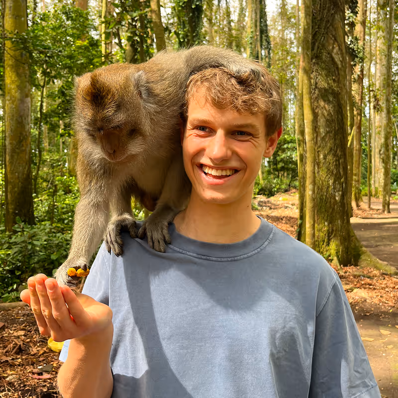 Manuel Schneider im Wald mit einem Affen auf der Schulter, der aus seiner Hand isst.
