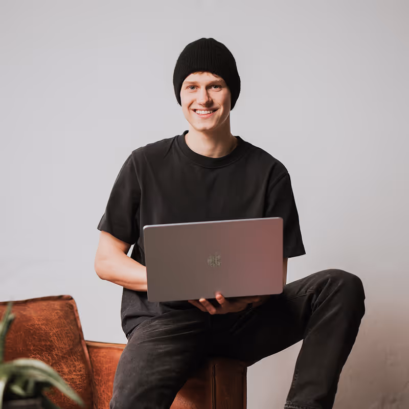 Webdesigner & Webflow Entwickler Manuel Schneider sitzt lächelnd und entspannt mit einem Laptop auf dem Schoß.