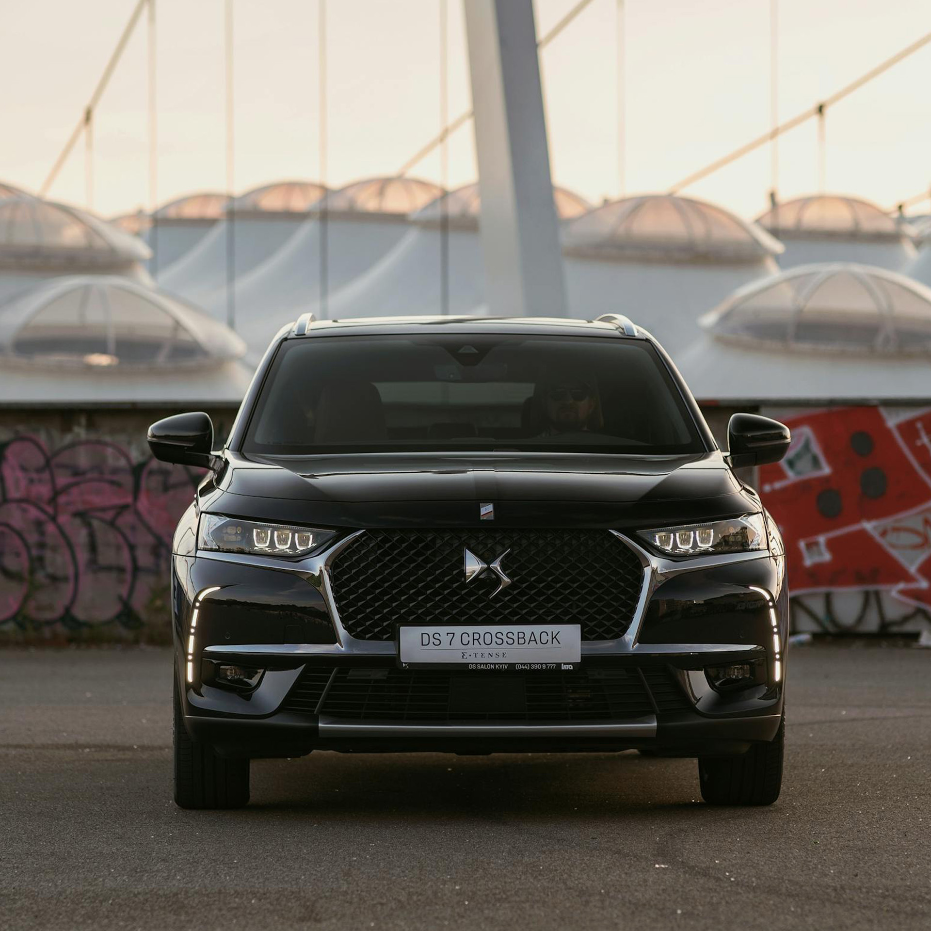 Front view of a black DS 7 Crossback car parked on a street with graffiti-covered walls in the background.