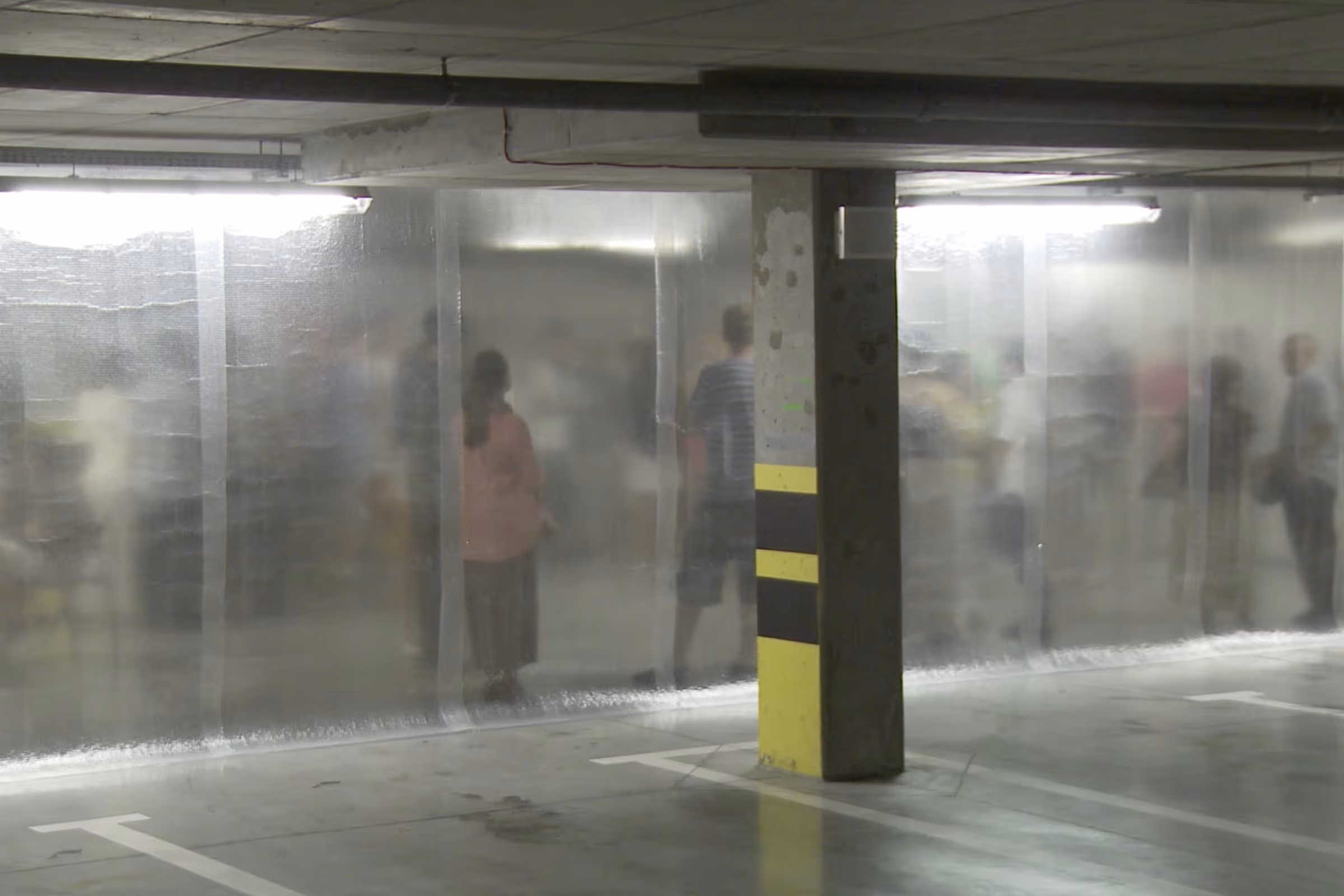People standing behind translucent plastic curtains in an indoor parking garage.