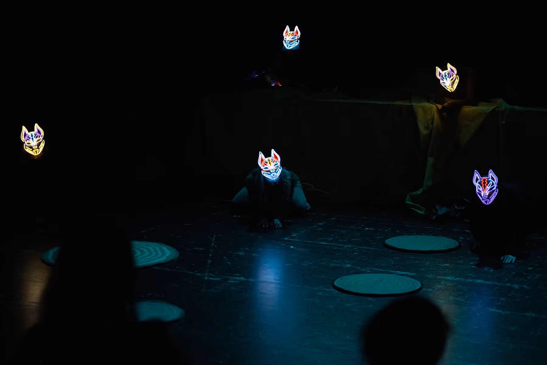 Person wearing a fur coat and tiara crouched on a stage with yellow fabric around them against a dark background.