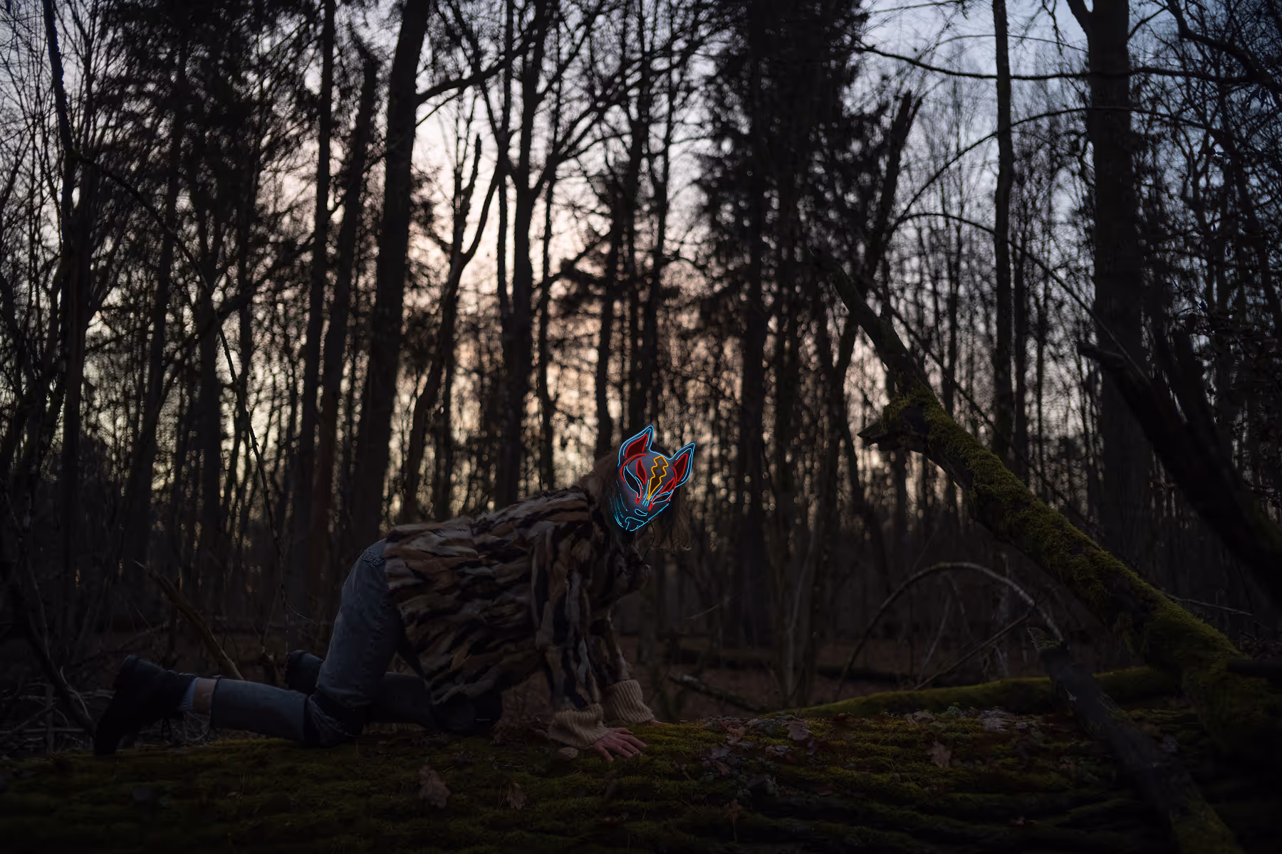 Person wearing a neon-lit fox mask and camouflage jacket crouching on a mossy log in a dark forest at dusk.