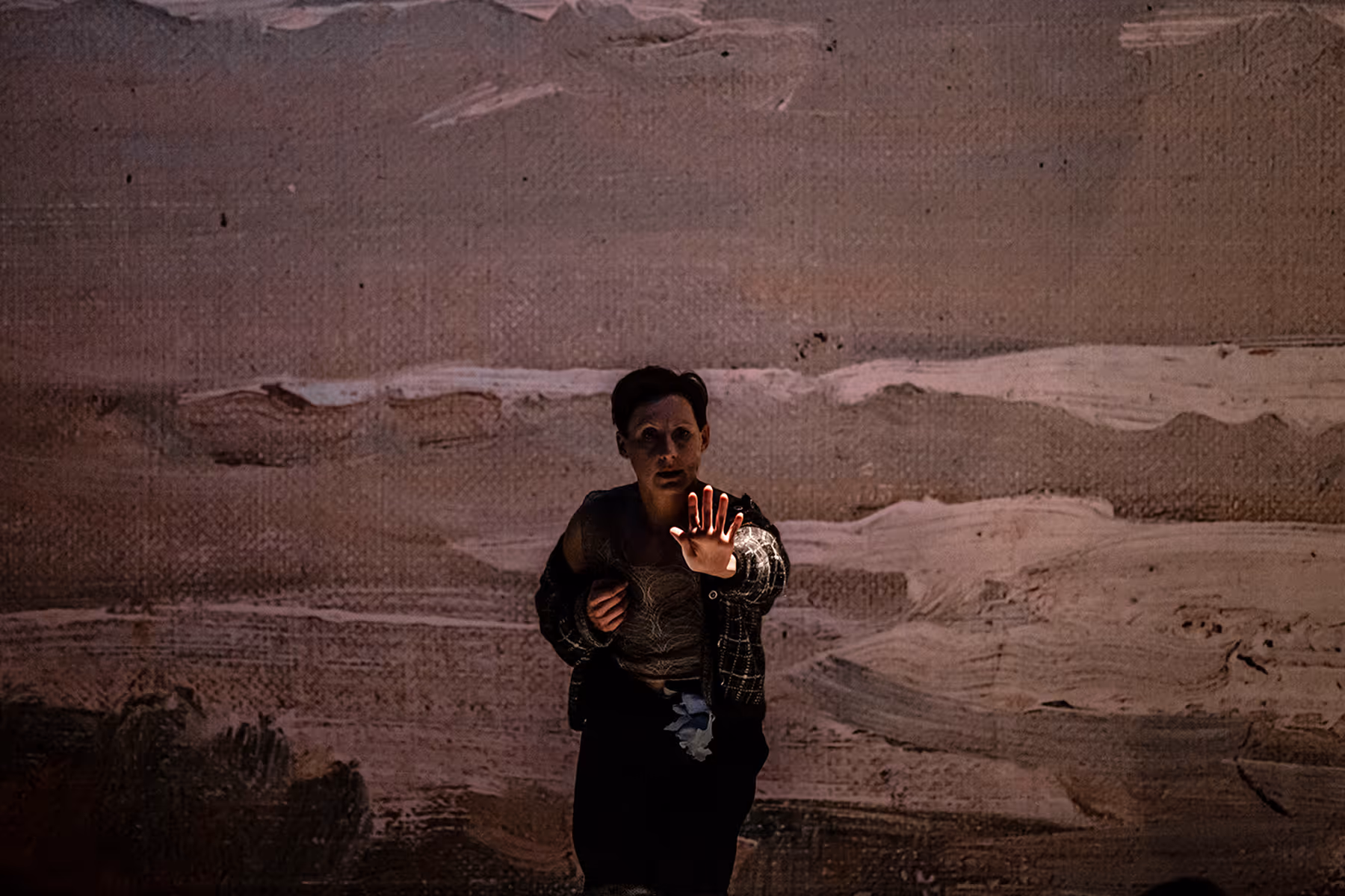 Person with short hair in dark clothing extends a hand forward against a textured, abstract backdrop.