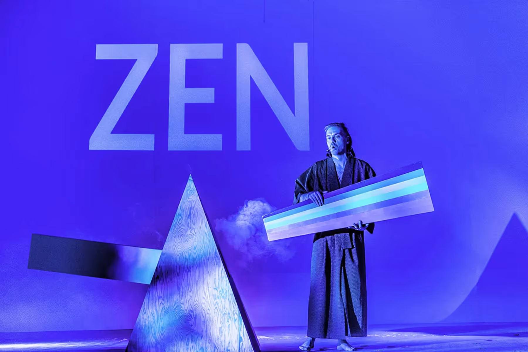 Four people dressed in dark clothing standing under a large crumpled silver foil structure, looking towards the illuminated sign reading 'WAMPIR' on a blue wall.